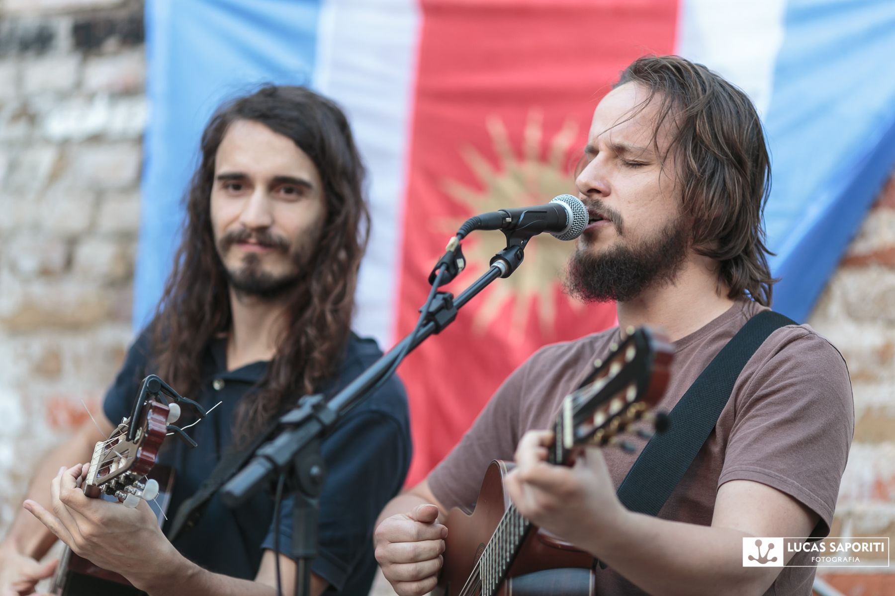 Dois violonistas cantam lado a lado diante da bandeira de Santiago del Estero