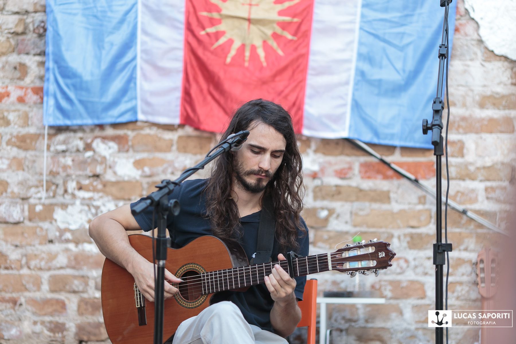 Marcos Saporiti canta com o violão diante da bandeira de Santiago del Estero